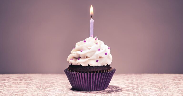 A single cupcake with a single lit candle on a decorative background